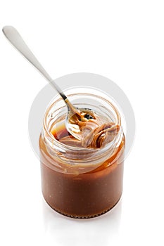 Spoon with salted caramel sauce on jar isolated on white