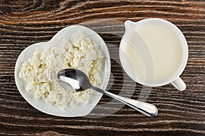 Spoon on saucer in heart shape with cottage cheese, pitcher with yogurt on table. Top view