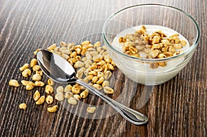 Spoon on scattered puffed wheat, bowl with yogurt and puffed wheat on wooden table