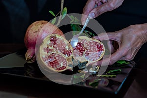 spoon scooping out grains of pomegranate fruit on a table
