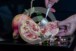 spoon scooping out grains of pomegranate fruit on a table