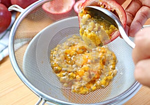 Spoon Scooping Passion Fruit Flesh into Strainer to Extract Liquid from the Pulps for Making Puree