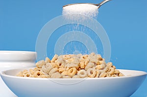 Spoon sprinkling sugar on a bowl of oat cereal on blue background