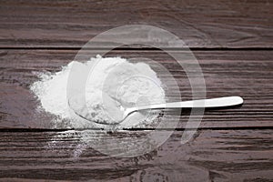 Spoon and sweet powdered fructose on black wooden table