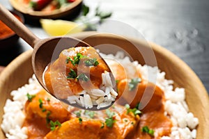 Spoon with tasty butter chicken over bowl of meal