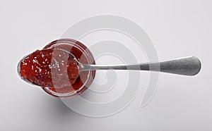 Spoon with tasty canned raspberry jam on jar against white background, top view