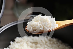 Spoon with tasty hot rice over cooker