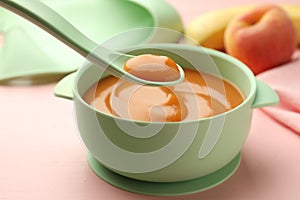 Spoon with tasty pureed baby food over bowl on pink wooden table, closeup