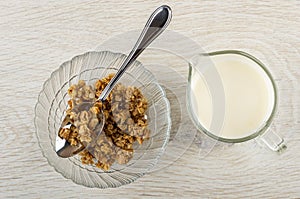 Spoon in transparent bowl with muesli, pitcher with yogurt on table. Top view