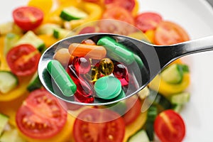 Spoon with weight loss pills over plate with vegetable salad