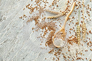 Spoon with wheat flour and grains on wooden background