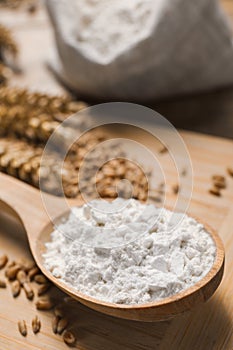 Spoon with wheat flour and grains on wooden board, closeup