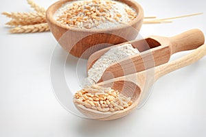 Spoon with wheat grains and scoop with flour on white background