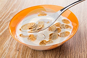 Spoon with yogurt, multicereal flakes above bowl on table