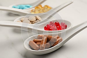 Spoons with different dietary supplements on white table, closeup