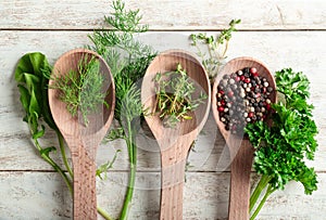 Spoons with different fresh herbs and spices on wooden background