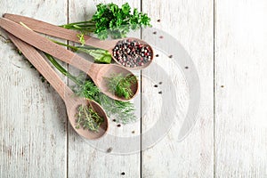 Spoons with different fresh herbs and spices on wooden background