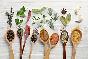 Spoons with different spices and herbs on white wooden table, flat lay