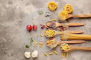 Spoons with different types of raw pasta on grey background