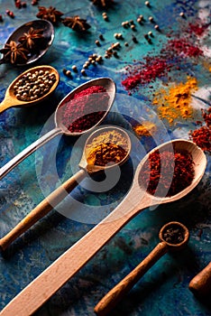 Spoons with spices on a colored concrete background