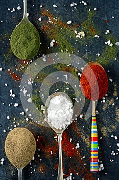 Spoons with spices and salt on black background sprinkled with different kind of spices