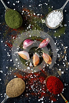 Spoons with spices and salt on black background sprinkled with different kind of spices