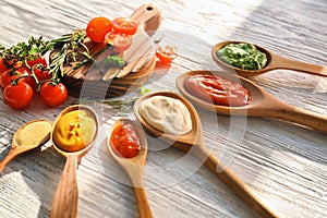 Spoons with tasty sauces on white wooden table photo