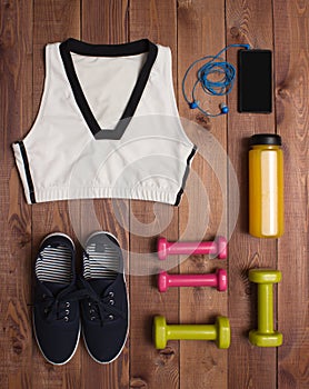 Sport accessories: clothes, shoes, weights, bottle, phone on wooden background