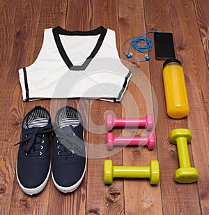 Sport accessories: clothes, shoes, weights, bottle, phone on wooden background