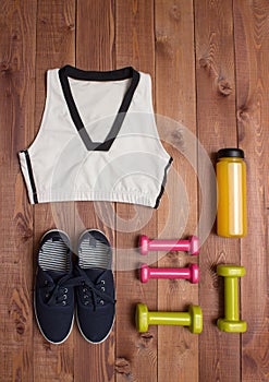 Sport accessories: clothes, shoes, weights, bottle on wooden background