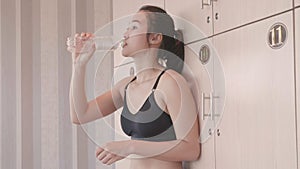 Sport Asian woman opening private locker in locker room and putting drinking pure water bottle after relax breaking from workout