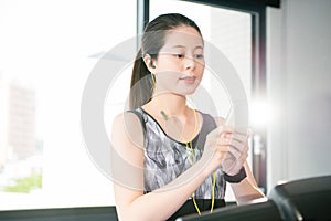 Sport asian woman running treadmill use smartphone listening mus