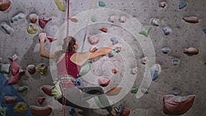 Sport athletic woman climbing rock climbing wall, practicing solo in indoor gym. An experienced girl is wearing a safety
