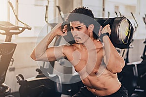 Sport background of caucasian young man having workout in gym center or fitness club with weights bag lifting on shoulder