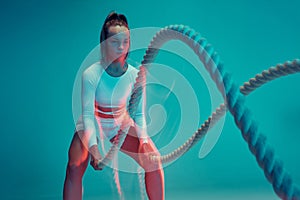 Sport backgrounds. Powerful attractive woman fitness trainer do battle workout with ropes at the studio on blue