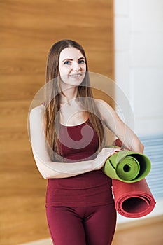 Sport beautiful smiling woman in red sportswear with red and green mats for yoga in the gym and looking at the camera. Healthy lif