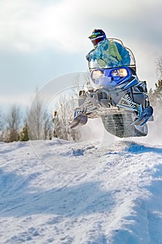 Sport blue snowmobile jump. Cloud of snow dust from under snowmobile tracks. Front view, vertical shot. photo