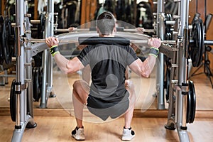 Sport, bodybuilding, lifestyle and people concept - young man with barbell doing squats in gym.