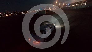Sport car drifting on asphalt road in night city aerial shooting. Fpv freestyle drone view white jdm racing vehicle