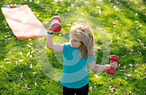 Sport children. Cute little boy doing exercises with dumbbells in green park. Portrait of sporty child with dumbbells