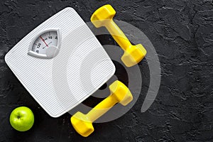 Sport and diet for losing weight. Bathroom scale, apple and dumbbell on black background top view copyspace