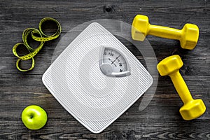 Sport and diet for losing weight. Bathroom scale, apple and dumbbell on wooden background top view