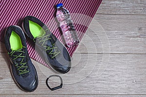 Sport equipment with sport shoes, pilates mat, smart watch and bottle of water on a wooden floor