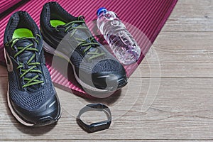 Sport equipment with sport shoes, pilates mat, smart watch and bottle of water on a wooden floor