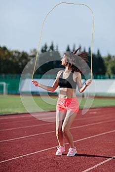 Sport, exercises outdoors. woman in black top and rose shorts jumping on skipping rope on stadium. Sporty girl in good shape, full