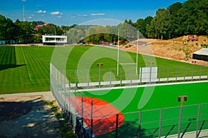 Sport field for soccer or rugby infrastructure with vibrant green grass and gate, outskirts of the city space, summer sunny clear