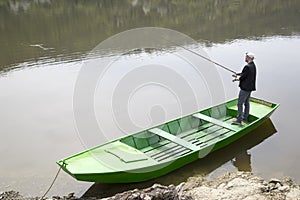 Sport Fisherman Holding Fishing Rod And Fishing From The Green Boat