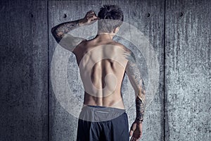 Sport fit muscular tattooed guy from back in loft space