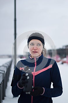 Sport fitnes girl drinks water on jogging outside at cloudy winter day