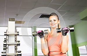 Sport, fitness, bodybuilding, teamwork and people concept - young woman flexing muscles on gym machine